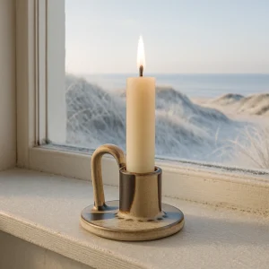 Nordischer Keramik-Kerzenhalter mit angezündeter Kerze auf Fensterbank, Winterlandschaft mit Dünen und Meer im Hintergrund