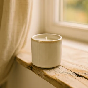 Wikholmform Alvy Kerze klein in heller, beiger Keramik auf rustikaler Fensterbank, sanftes Tageslicht und natürliche, nordische Wohnatmosphäre.