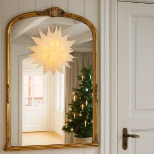 Leuchtender weißer Papierstern „Linea“ im skandinavischen Wohnambiente, reflektiert in einem goldenen Spiegel mit Blick auf nordisch geschmückten Weihnachtsbaum