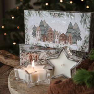 Zwei sternförmige Duftkerzen in Glas vor einer weihnachtlichen Geschenkbox, warme Winterstimmung