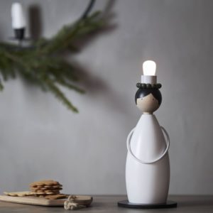 Fensterleuchter Lucia Classic aus weiß lackiertem Holz, stilisierte Lucia-Figur mit Kranz und E14-Fassung, ca. 12×26 cm, auf rundem schwarzen Standfuß.