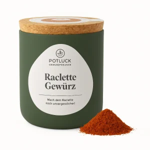 Grüne Potluck-Dose mit der Aufschrift ‚Raclette Gewürz‘ und Korkdeckel, daneben ein kleiner Haufen roten Gewürzpulvers, freigestellt auf weißem Hintergrund.