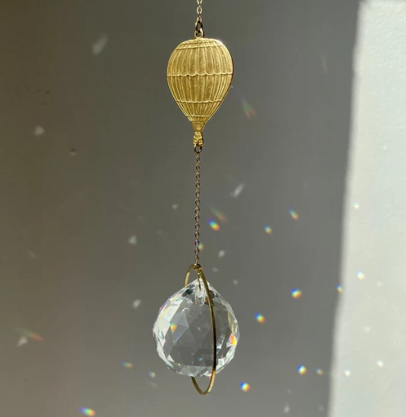 Goldfarbener Suncatcher Ballon mit Kristallglas-Prisma und Regenbogenreflexen am Fenster