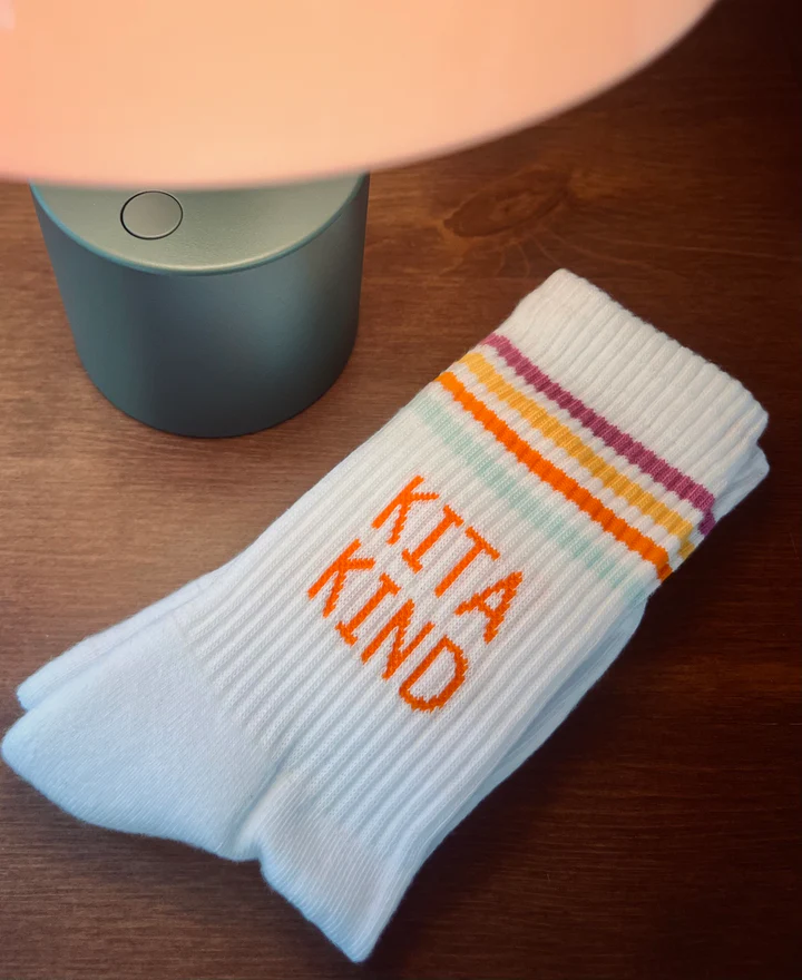Weiße Kita Kind Socken von Loones mit Pastellstreifen und orangefarbenem Schriftzug